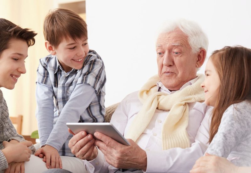 Children looking at grandpa holding a tablet